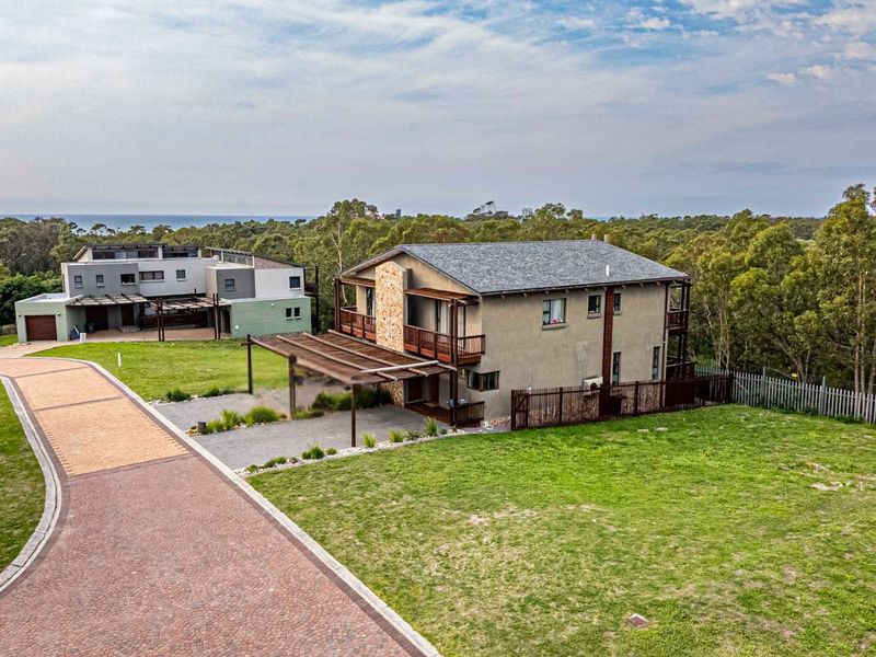 Aerial view of a residential property featuring a multi-story home with a wooden pergola, balcony, and landscaped surroundings in a quiet estate setting.