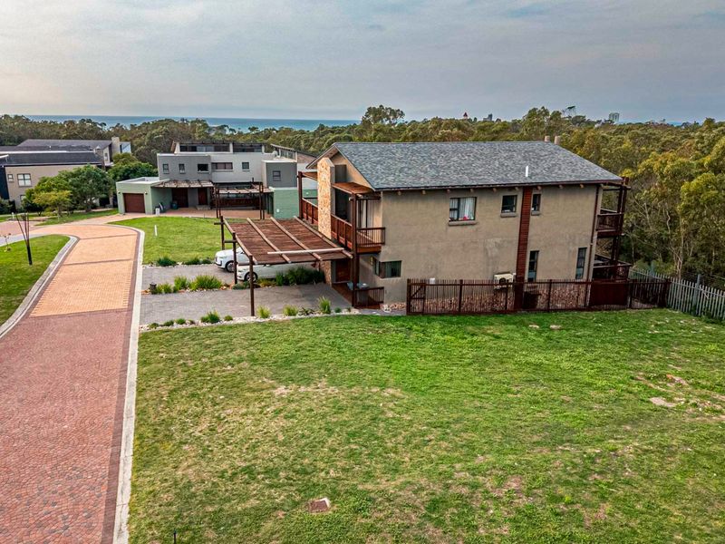 Aerial view of a residential property featuring a multi-story home with a wooden pergola, paved driveway, and surrounding landscaped garden area.
