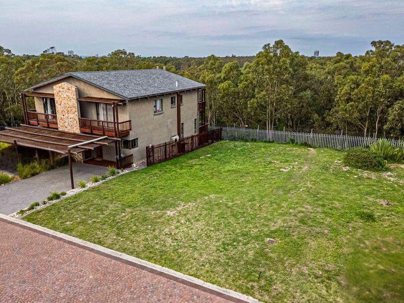 An aerial view of a residential property featuring a large grassed yard, paved driveway, and a multi-story dwelling with a covered patio area.