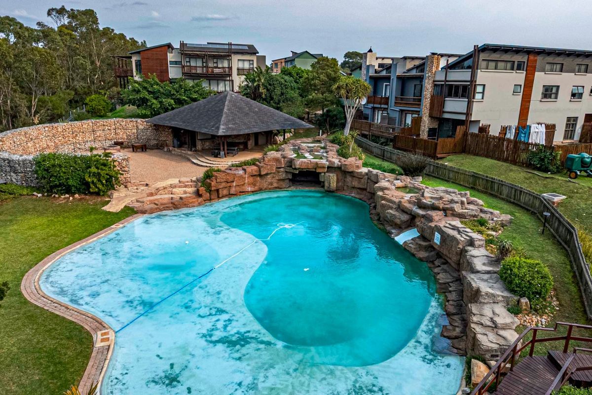 Aerial view of a landscaped residential pool area featuring a rock-feature swimming pool, stone retaining wall, and a covered outdoor entertainment pavilion.