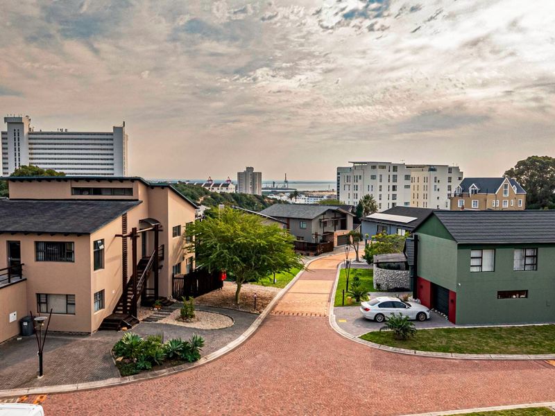 An elevated aerial view of a residential street within a developed estate, showcasing surrounding homes, paved roads, and distant coastal views.
