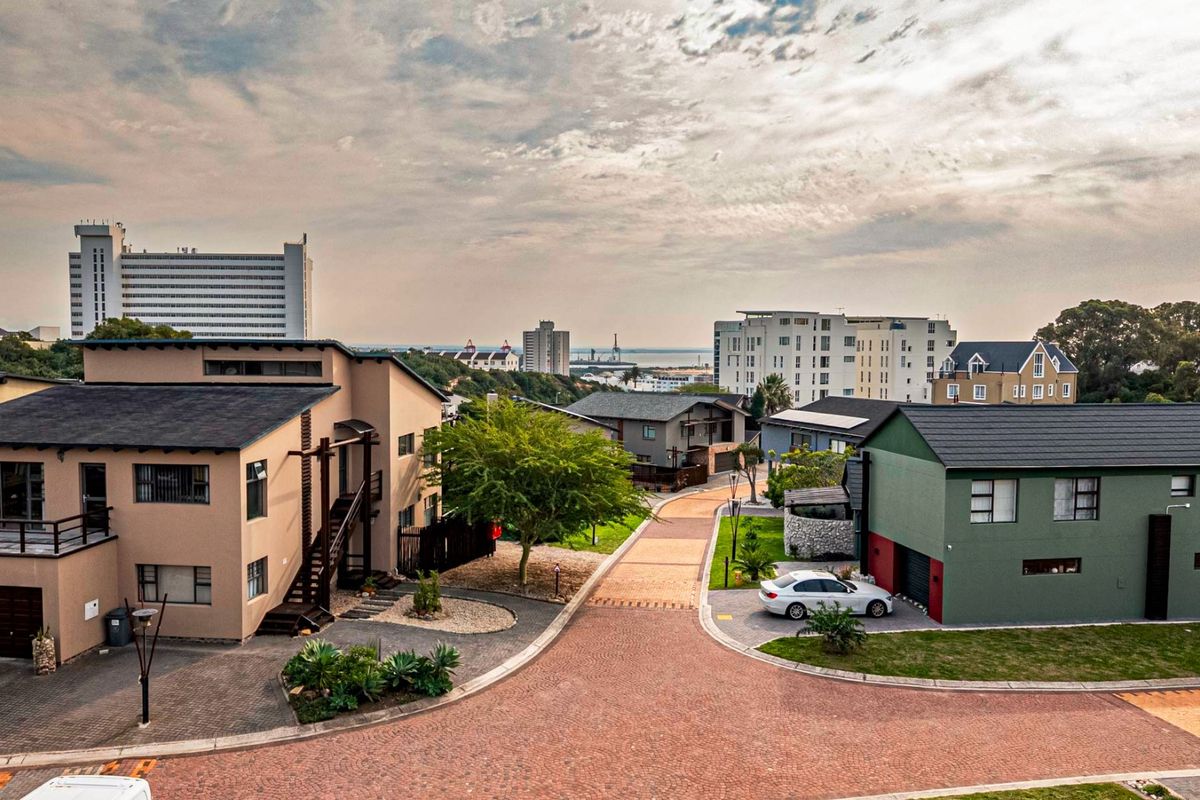 An elevated aerial view of a residential street within a developed estate, showcasing surrounding homes, paved roads, and distant coastal views.