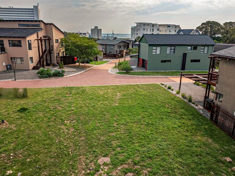 An elevated view of a vacant residential plot situated within a developed estate, featuring surrounding modern homes and paved access roads.