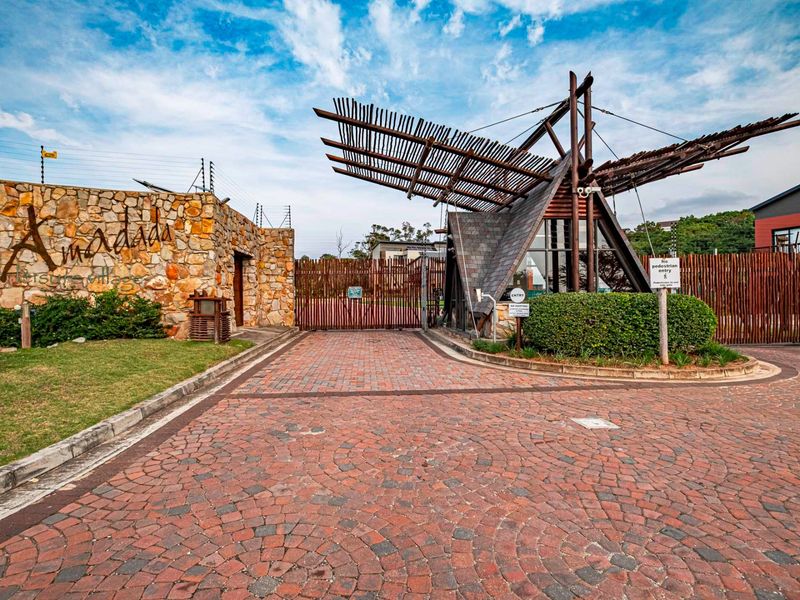 The secure entrance gate of Amadada Leisure Village, featuring stone masonry walls, a unique timber-slatted canopy, and paved driveway access.