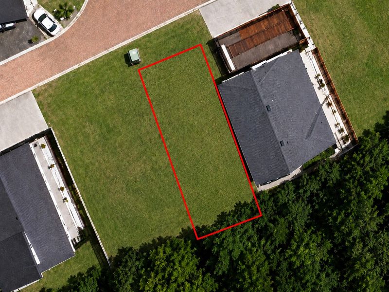 Aerial view of a vacant residential plot highlighted in red, situated between existing homes in a developed neighborhood.