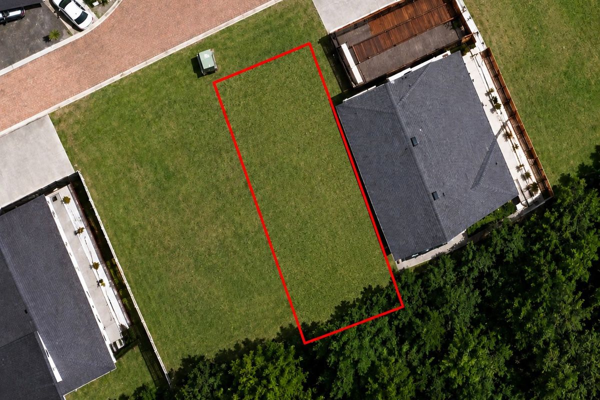 Aerial view of a vacant residential plot highlighted in red, situated between existing homes in a developed neighborhood.