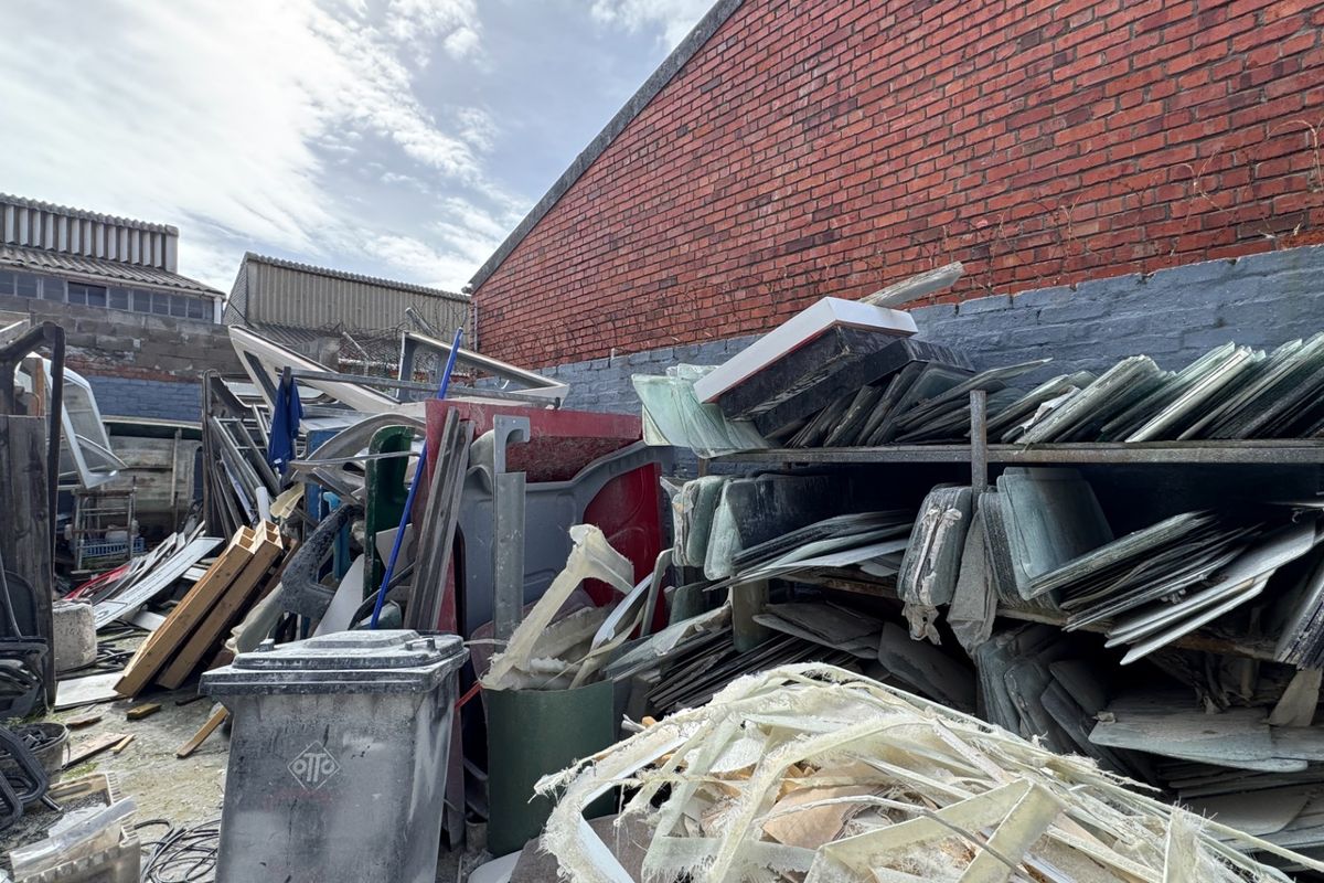An exterior industrial yard area featuring exposed brick walls and significant accumulation of stored materials and industrial debris.