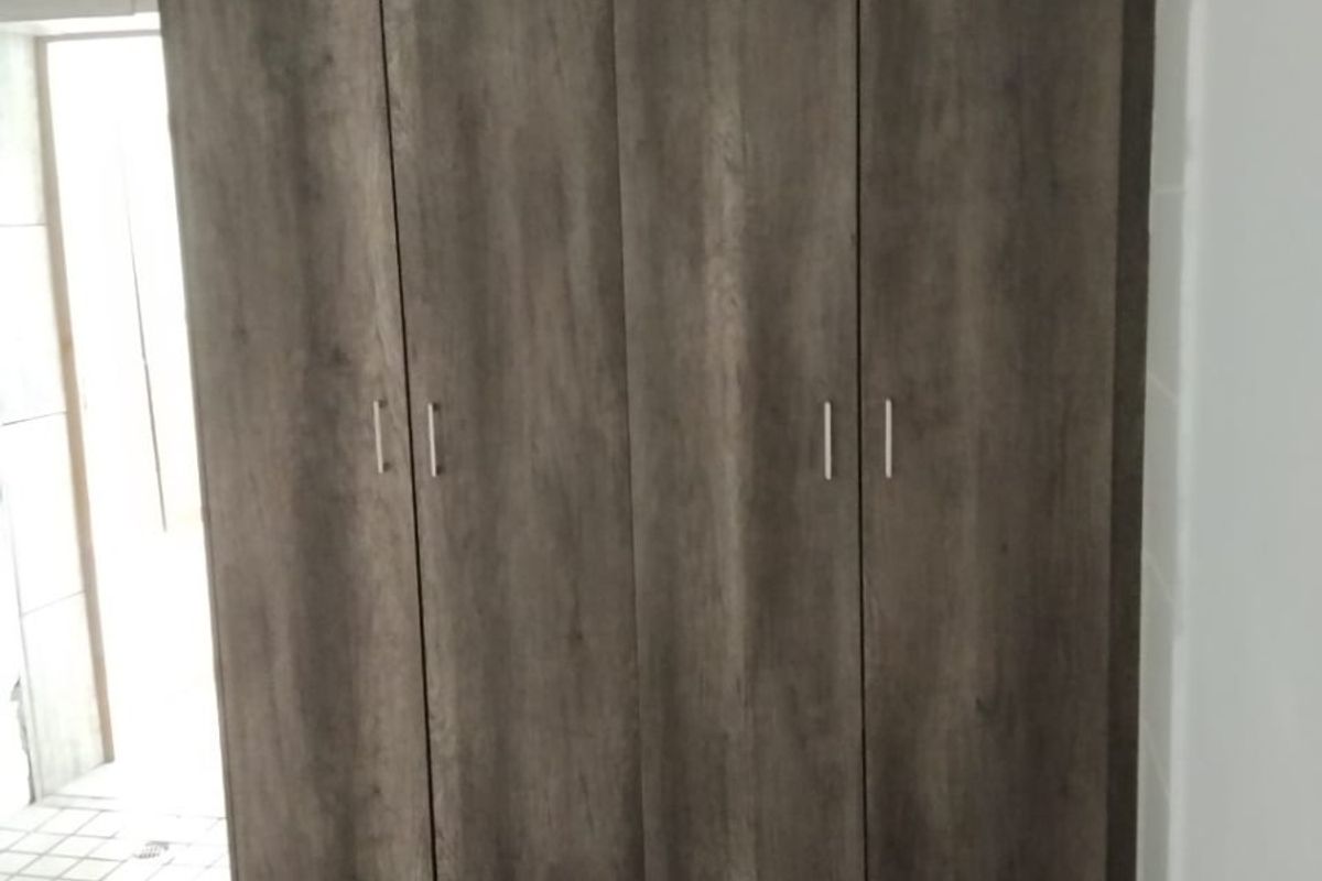 A bedroom featuring built-in wooden cupboards with a modern finish and tiled flooring.