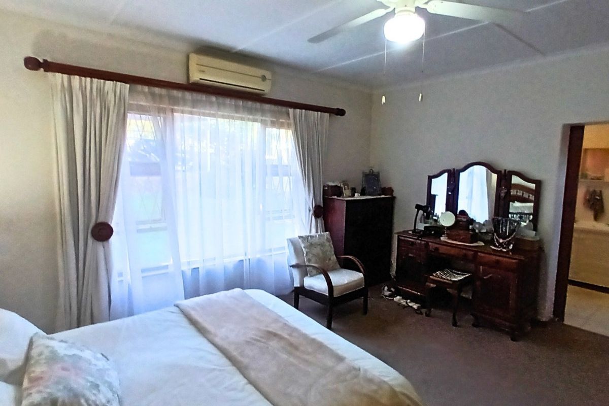 A bedroom featuring a ceiling fan, wall-mounted air conditioning unit, and an adjoining en-suite bathroom.
