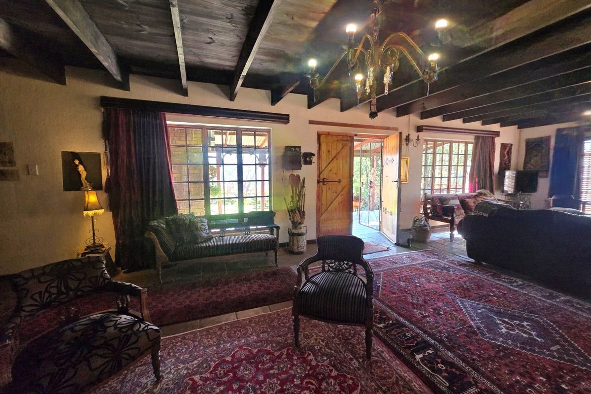 Spacious living room featuring exposed timber ceiling beams, tiled flooring, and large multi-pane windows providing natural light and access to the outdoor area.