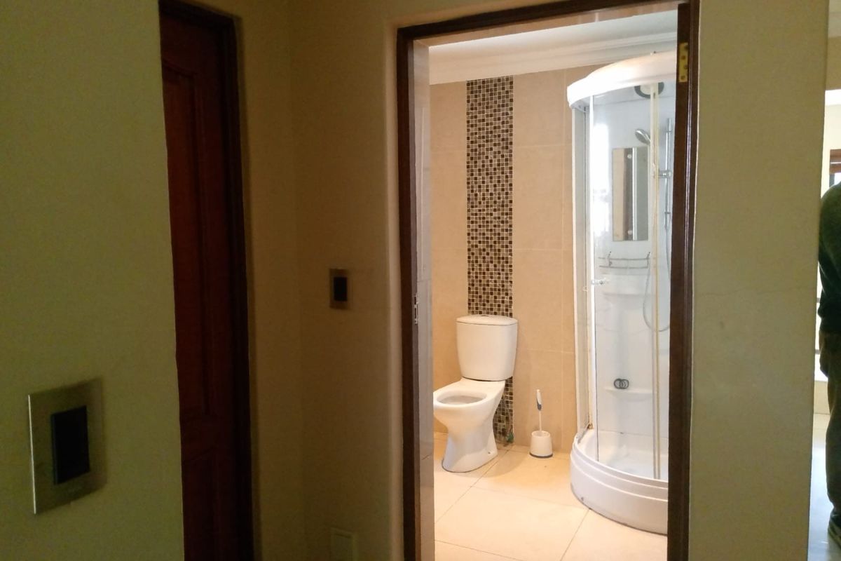 A view into a bathroom featuring a corner shower enclosure, a toilet, and decorative mosaic tile accents on the wall.