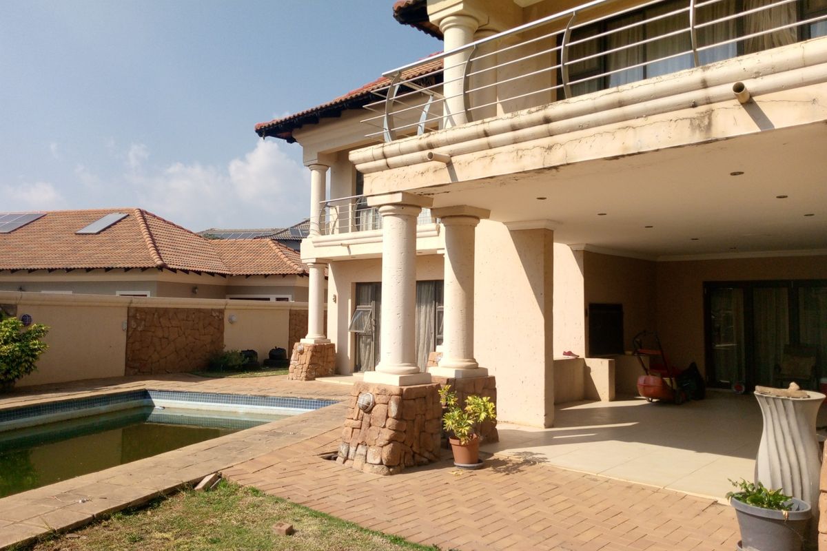 Rear view of a multi-story house featuring a covered patio, stone-clad columns, a balcony with stainless steel railings, and an adjacent swimming pool.