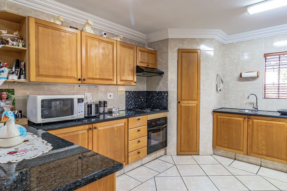 A functional kitchen featuring wooden cabinetry, granite countertops, a built-in oven with extractor fan, and tiled flooring.