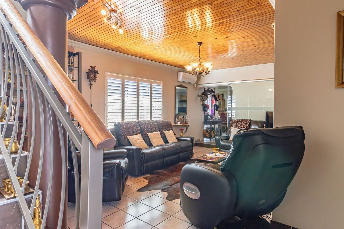Spacious living area featuring a distinctive timber-clad ceiling, tiled flooring, and an integrated staircase with a decorative metal balustrade.