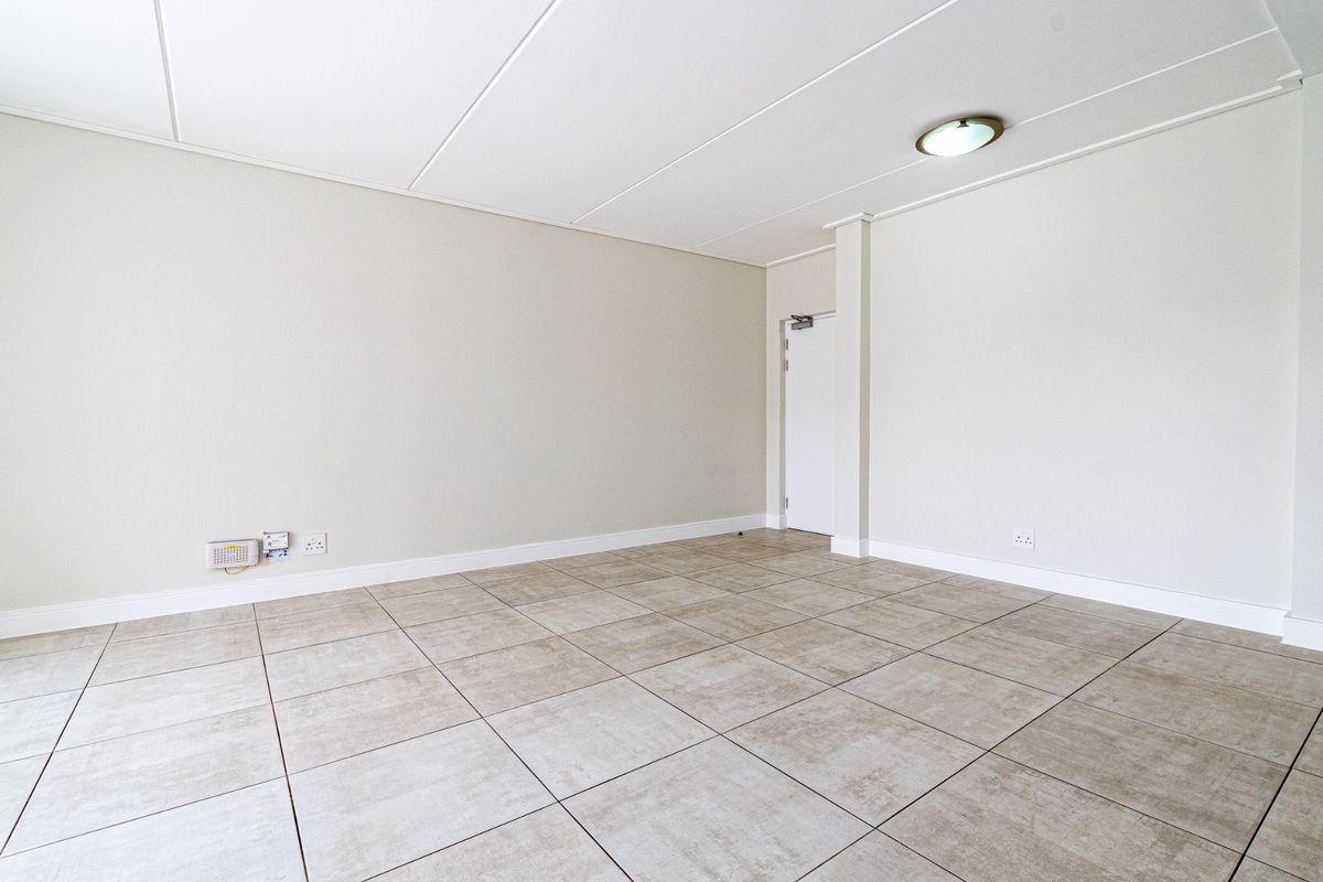 A bright, empty living area featuring neutral tiled flooring, clean white walls, and a simple flush mount ceiling light fixture.