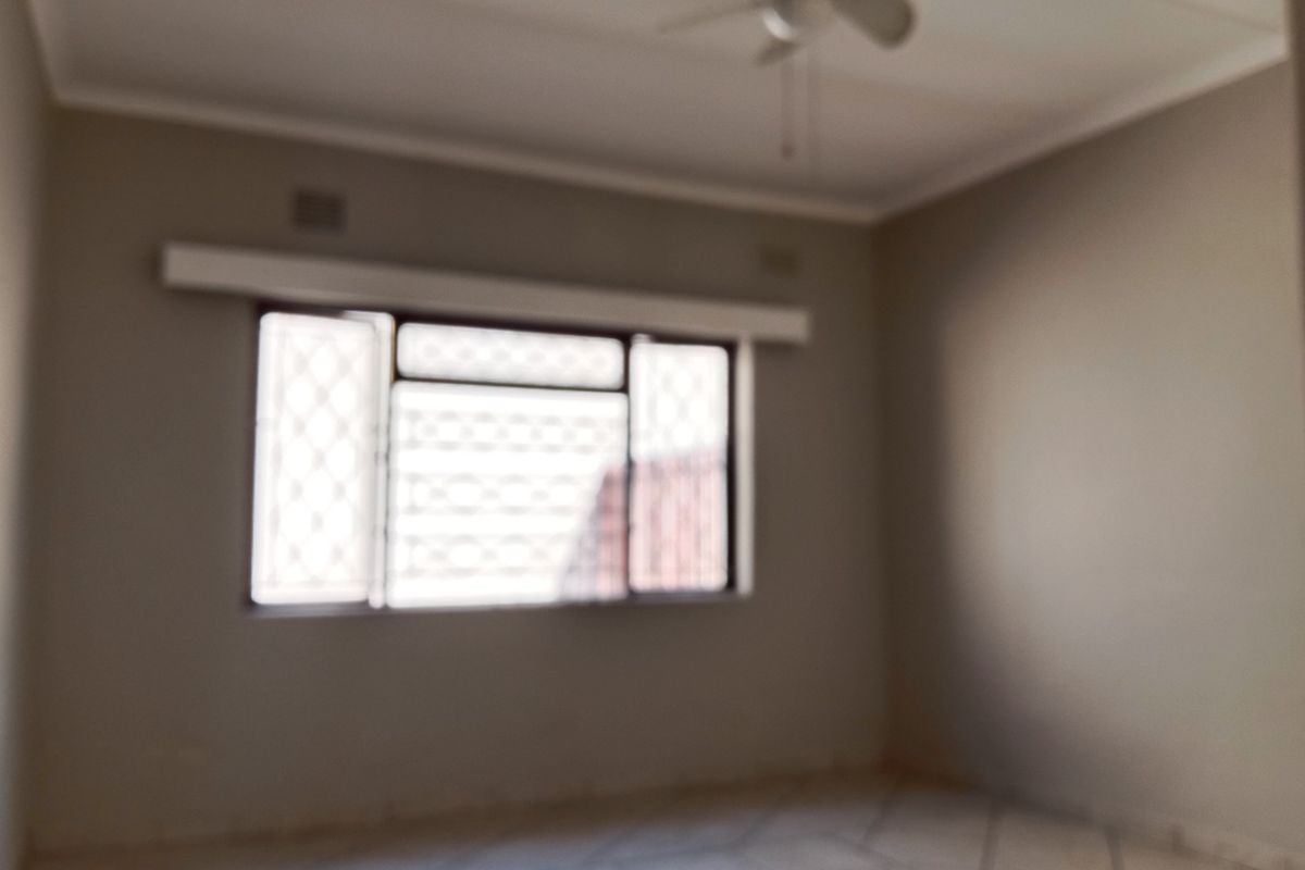 An empty bedroom featuring tiled flooring, a ceiling fan, and a window fitted with security bars.