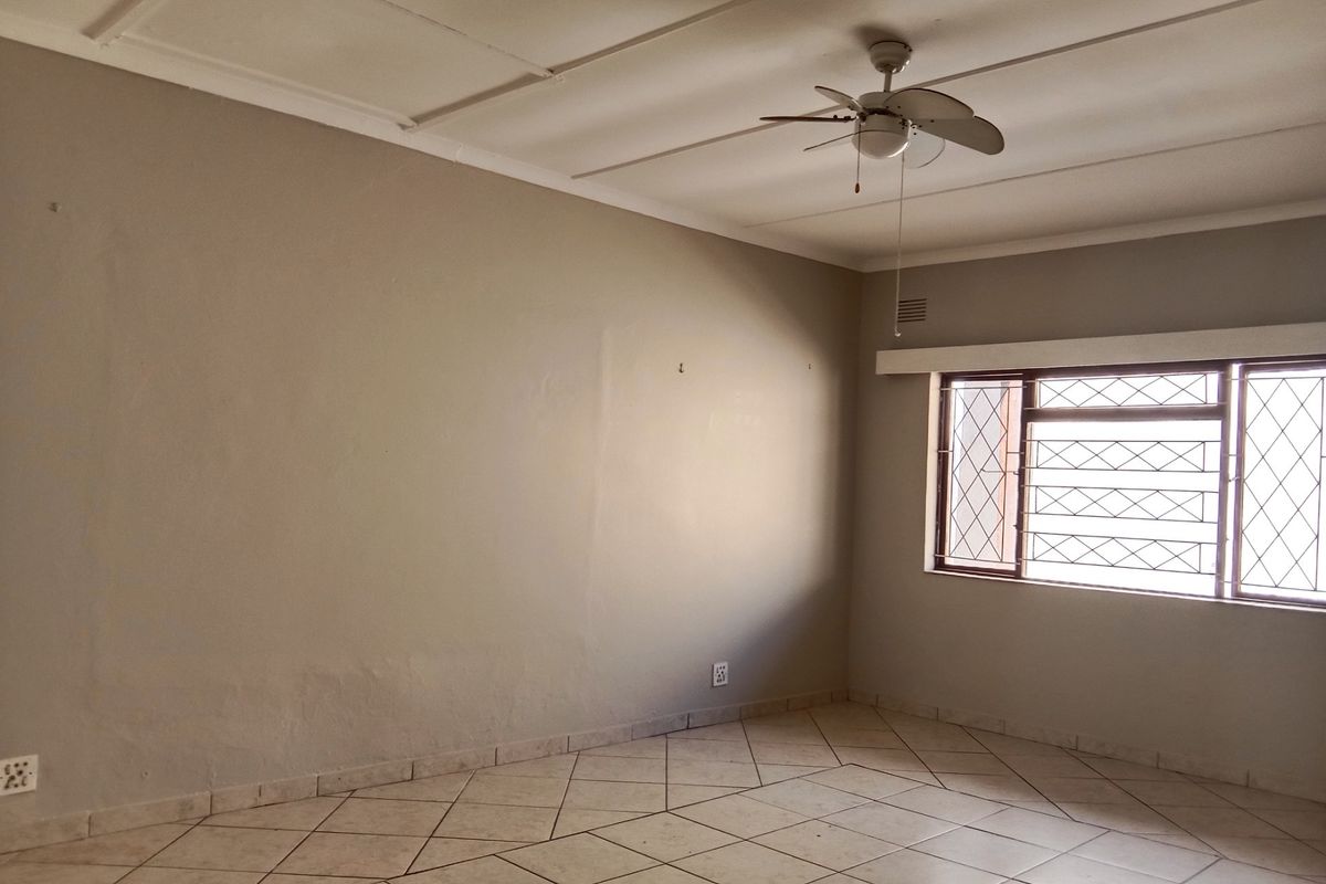 An empty living room featuring tiled flooring, a ceiling fan, and windows fitted with security bars.