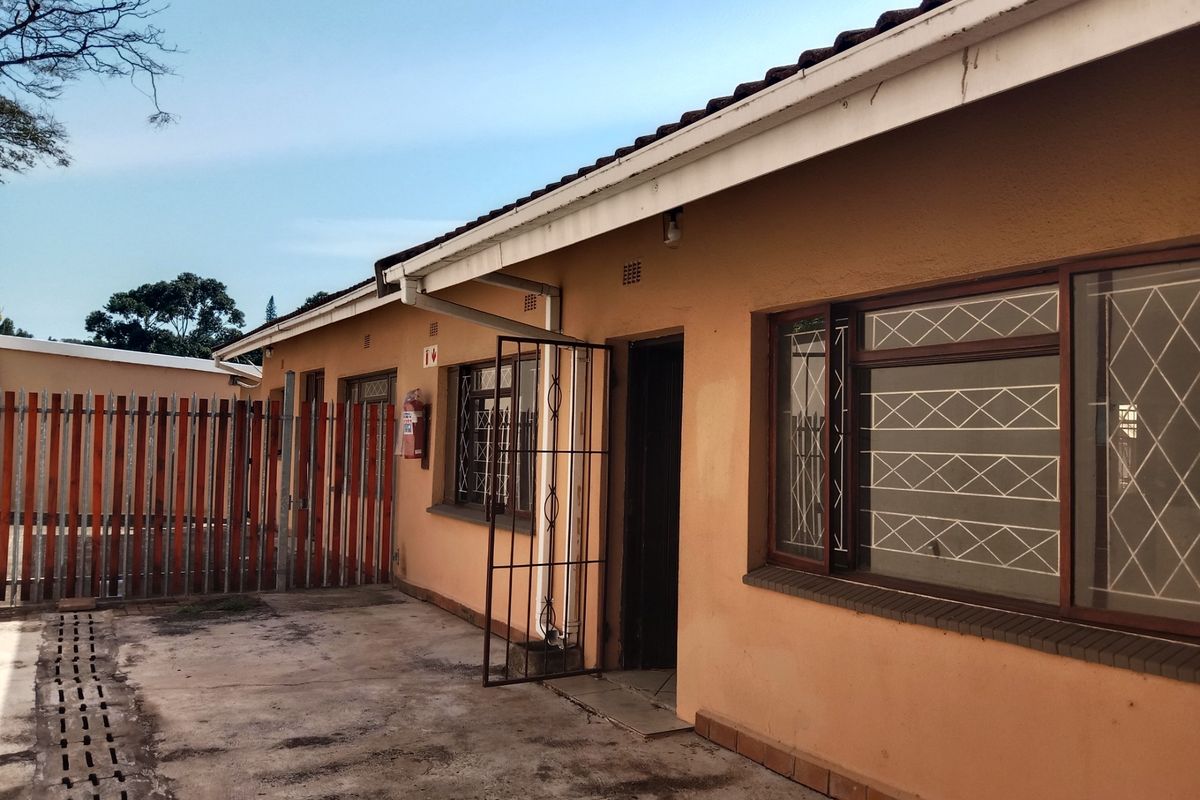 Rear exterior view of the apartment building featuring concrete paving, security gates, and security bars on the windows.