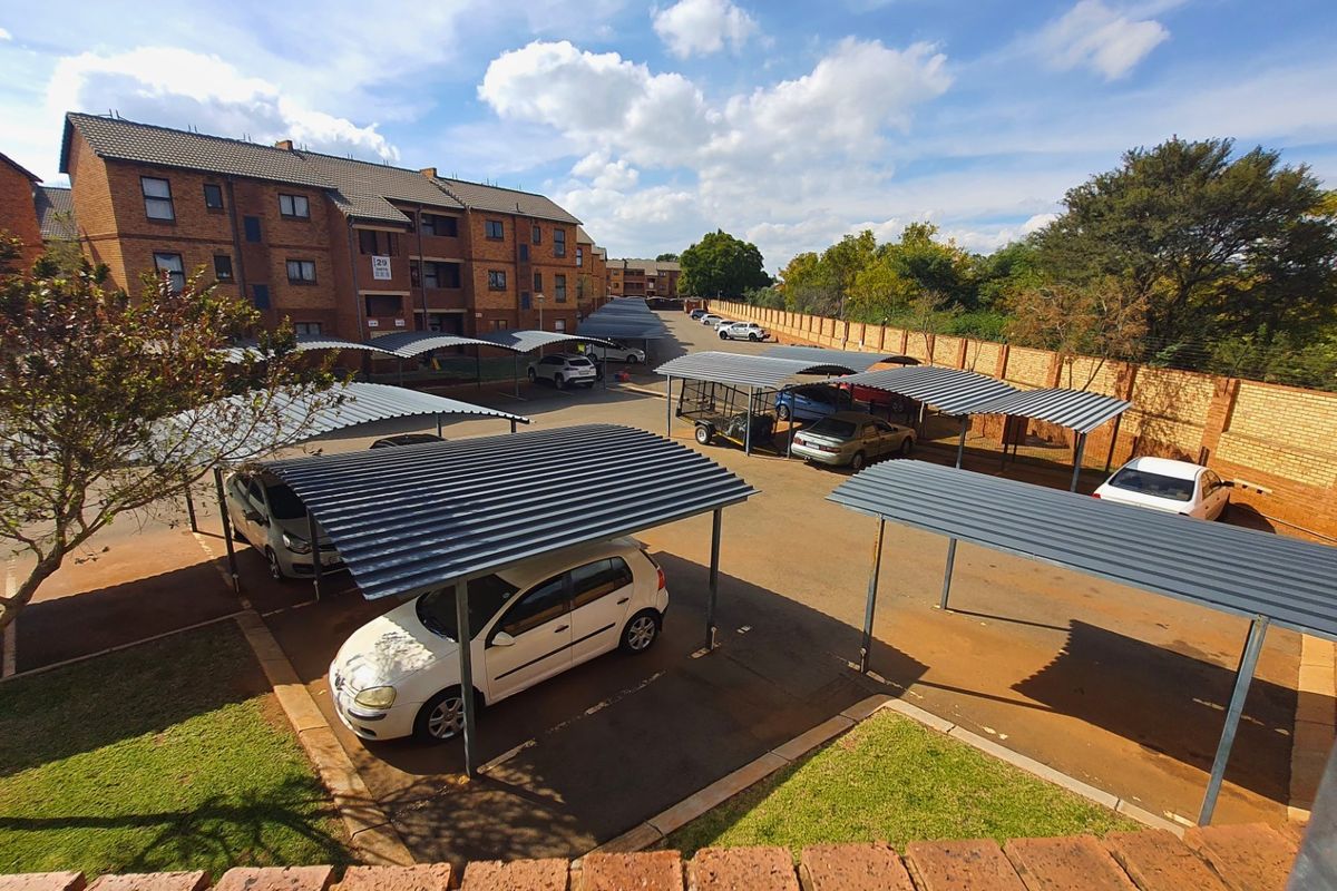 An elevated view of the apartment complex parking area featuring multiple covered carports, paved driveways, and perimeter brick boundary walls.