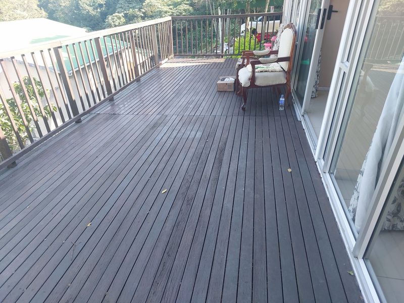 Spacious elevated timber balcony with wooden railings, offering an outdoor living area accessible through large sliding glass doors.