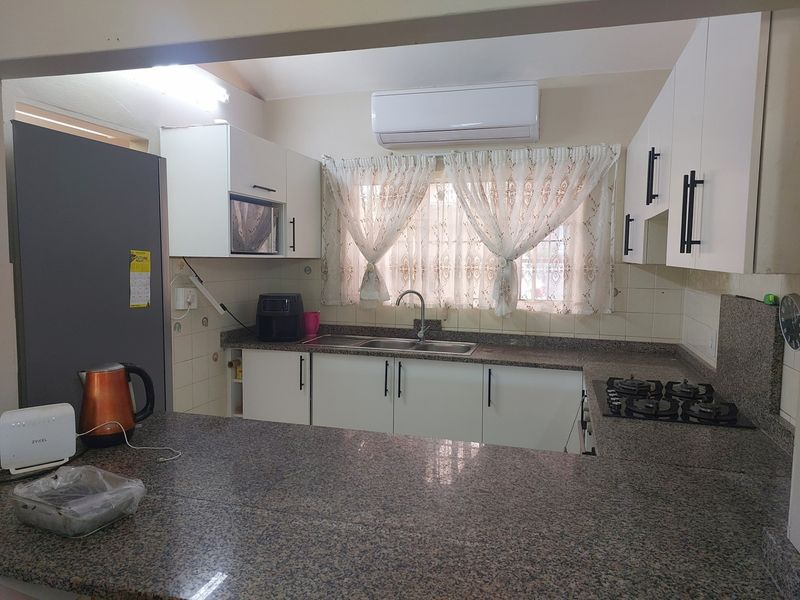 Functional kitchen featuring granite countertops, built-in gas hob, white cabinetry, and a wall-mounted air conditioning unit.