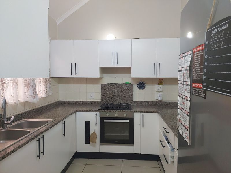 A functional U-shaped kitchen featuring white cabinetry, granite countertops, a built-in oven, gas hob, and a double stainless steel sink.