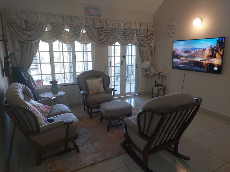 A cozy living room featuring tiled flooring, large windows with decorative curtains, and glass-paneled double doors leading to an outdoor area.