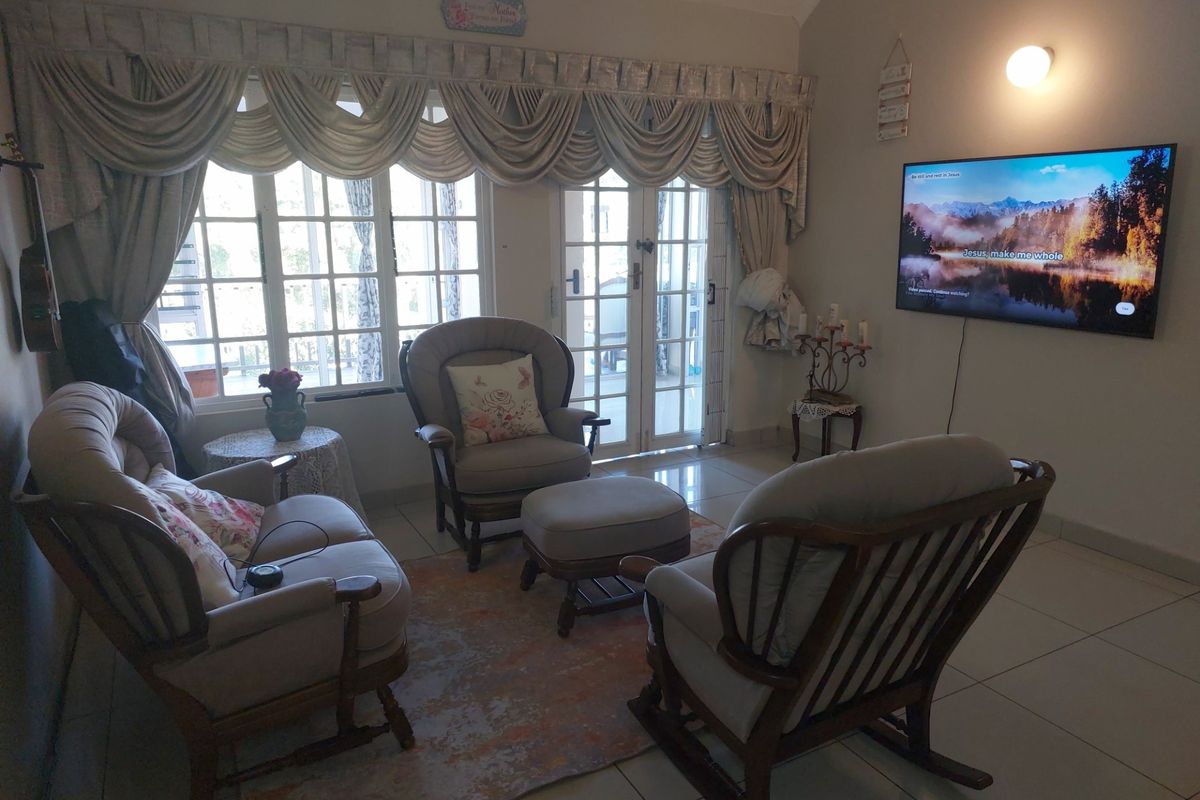 A cozy living room featuring tiled flooring, large windows with decorative curtains, and glass-paneled double doors leading to an outdoor area.