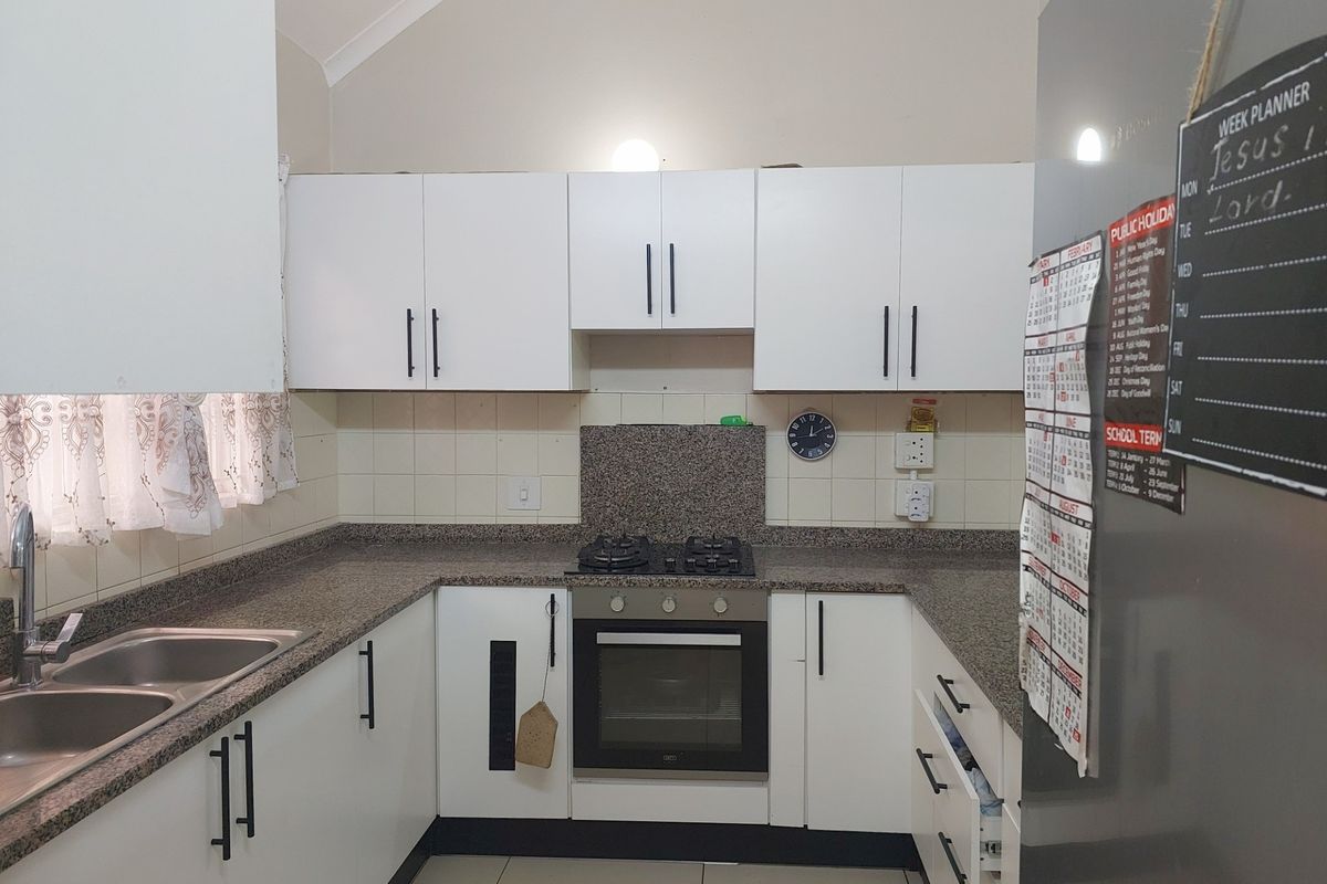 A functional U-shaped kitchen featuring white cabinetry, granite countertops, a built-in oven, gas hob, and a double stainless steel sink.