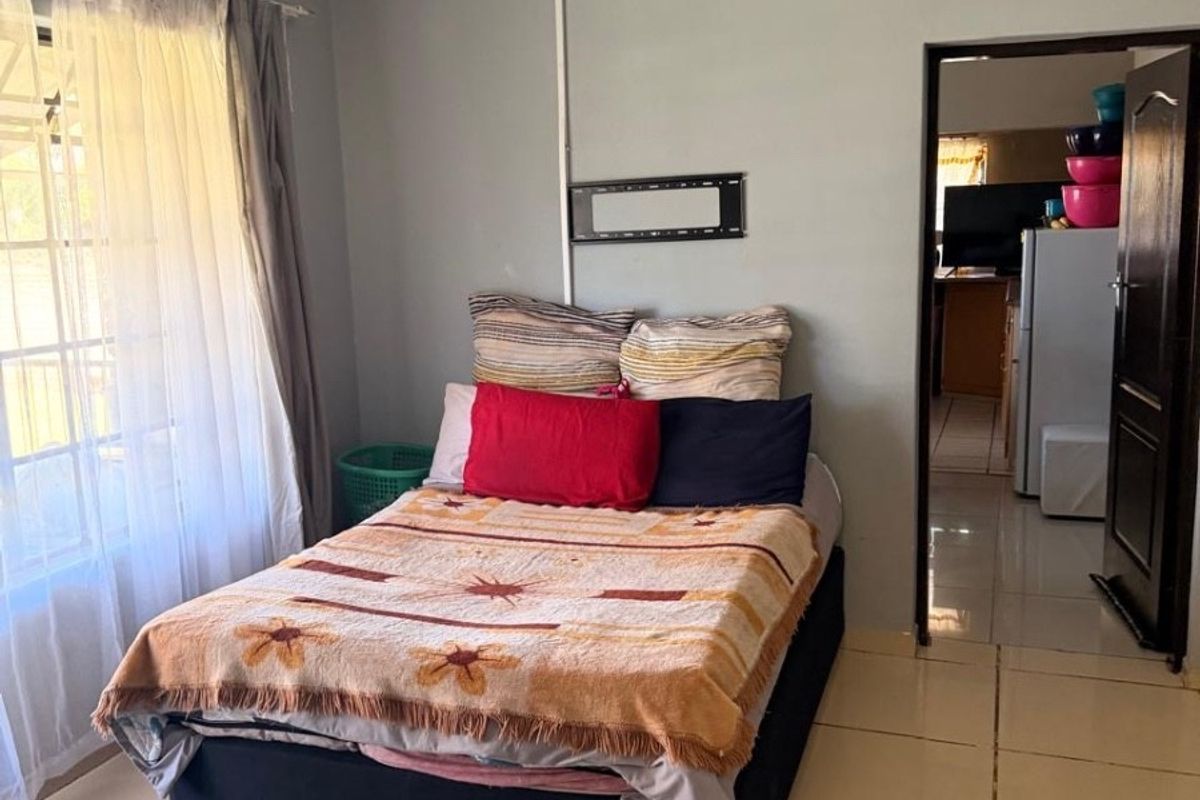 A bedroom featuring tiled flooring, a large window with natural light, and a doorway leading to an adjacent living area.