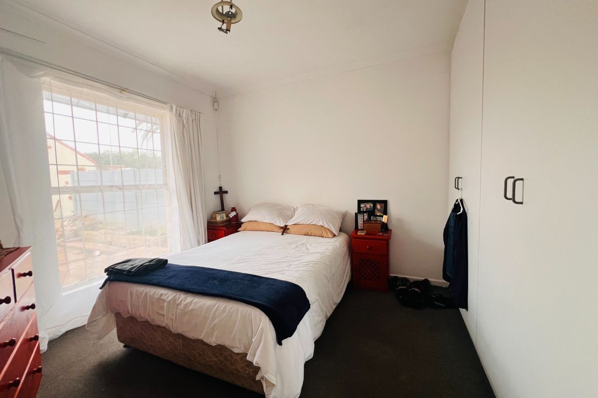 A bedroom featuring built-in wardrobes, dark carpeting, and a large window providing natural light.