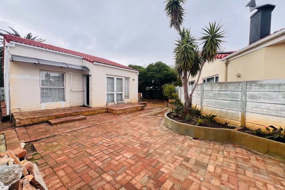 Rear exterior view of the property featuring a brick-paved courtyard, raised garden bed, and access to the main dwelling.