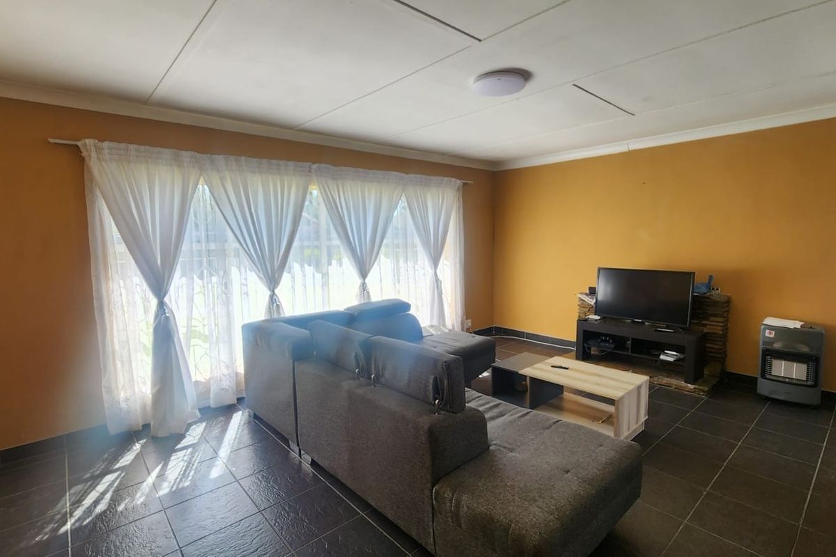 A spacious living room featuring dark tiled flooring, large windows with natural light, and a neutral layout suitable for various interior design styles.