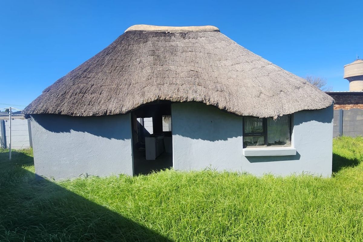 A detached structure featuring a traditional thatched roof, set within a large garden area with surrounding boundary walls.