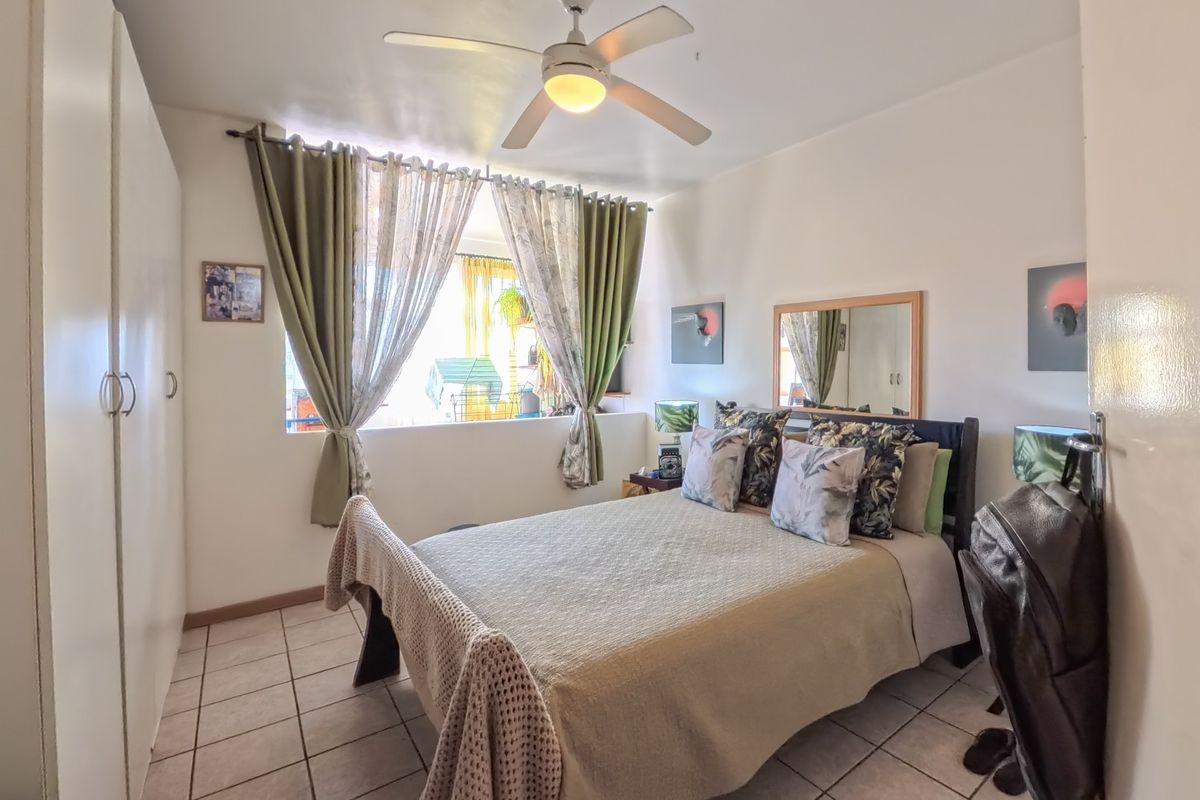 A bedroom featuring tiled flooring, a built-in wardrobe, and a ceiling fan, providing a functional and comfortable living space.