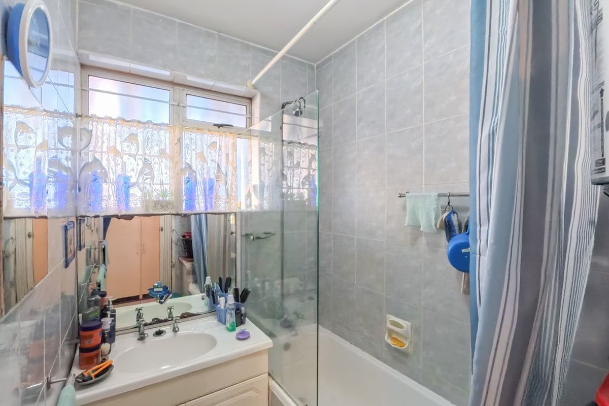A functional bathroom featuring a vanity basin, a bathtub with a glass shower screen, and tiled wall finishes.