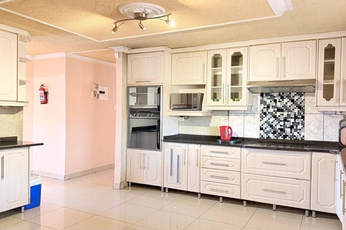 A functional kitchen featuring built-in cabinetry, integrated oven, microwave, and extractor fan with a tiled backsplash and polished floor tiles.