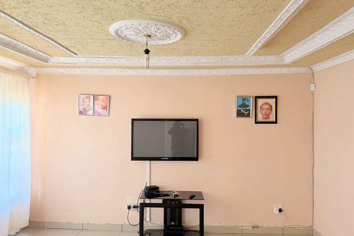 A living room featuring a textured ceiling with decorative molding, tiled flooring, and wall-mounted television setup.