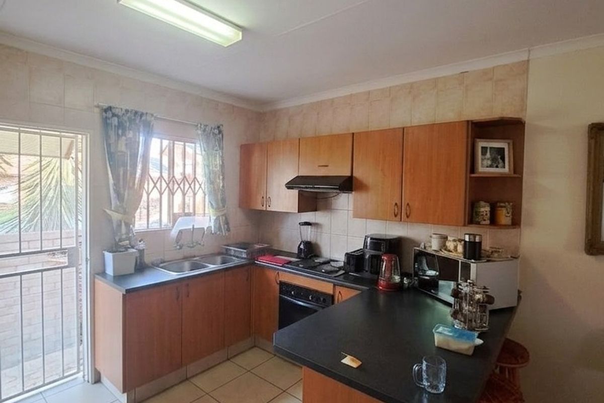 A functional kitchen featuring wood-finish cabinetry, a breakfast bar, tiled flooring, and direct access to an outdoor area through a security gate.