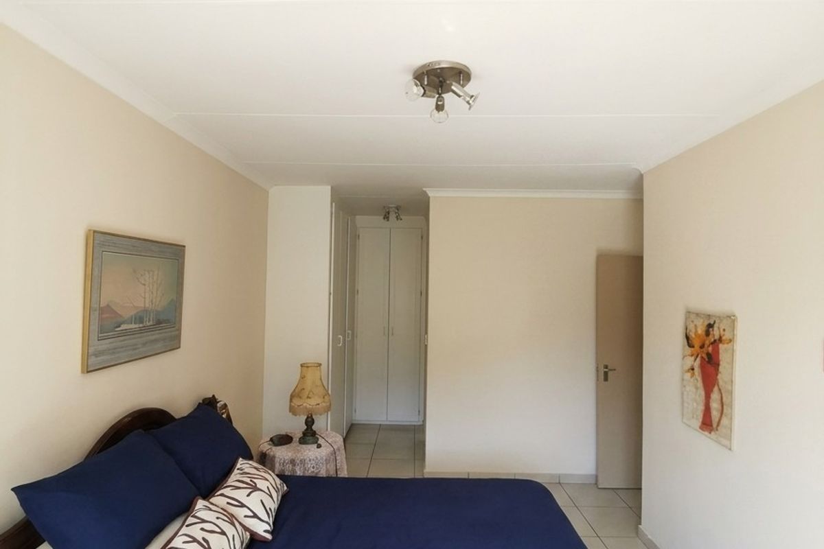 A well-lit bedroom featuring neutral wall tones, tiled flooring, and built-in cupboards, providing a clean and functional living space.