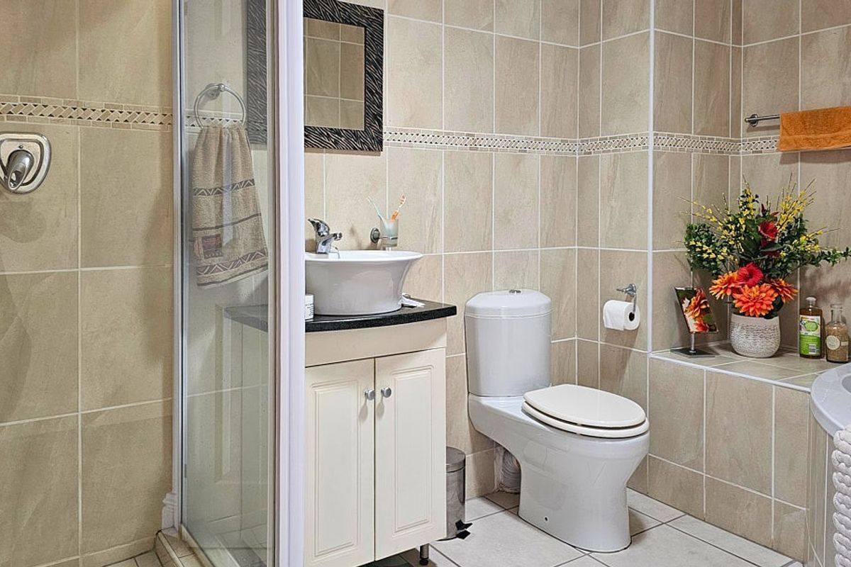 A compact bathroom featuring a glass-enclosed shower, a vessel sink vanity, a toilet, and tiled walls with decorative border accents.