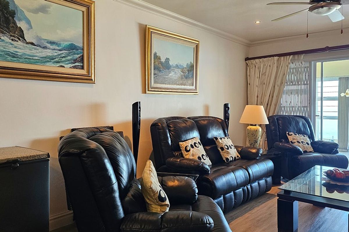 A comfortable living room featuring wood-look flooring, a ceiling fan, and sliding glass doors that open onto a balcony.