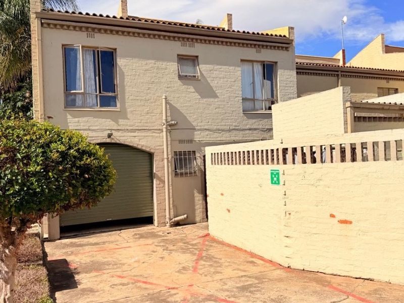 Exterior view of the apartment building featuring a private driveway, roller garage door, and a perimeter boundary wall.
