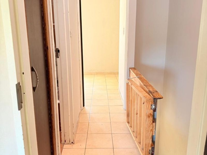 A narrow interior hallway featuring tiled flooring and a wooden safety gate, leading towards an adjacent room.