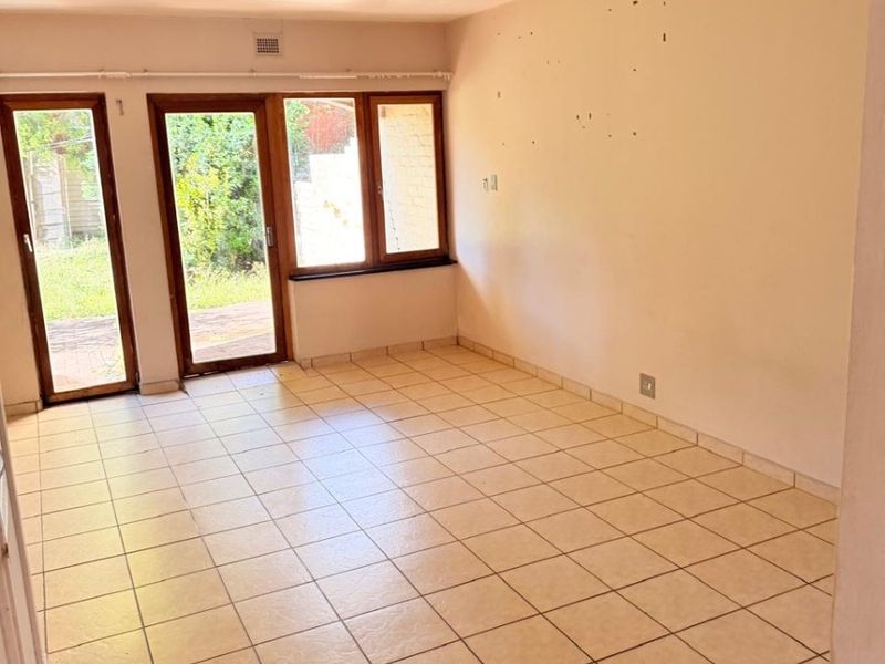 An empty living area featuring tiled flooring, a tongue-and-groove ceiling, and glass doors providing direct access to the outdoor space.