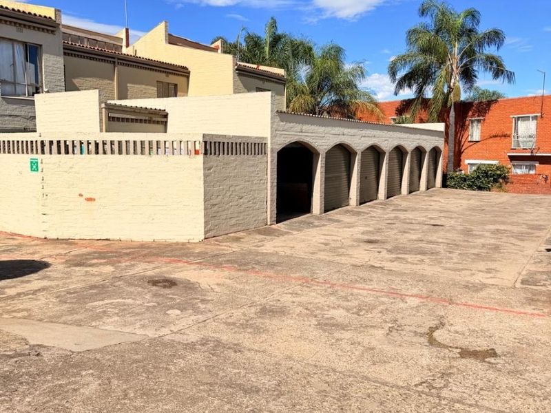 Exterior view of the apartment complex featuring a row of covered parking bays with arched brick detailing and a paved driveway area.