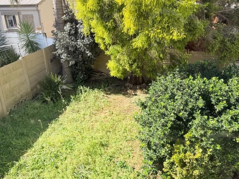 An elevated view of a private rear garden featuring established trees, shrubs, and a lawn area enclosed by perimeter boundary walls.
