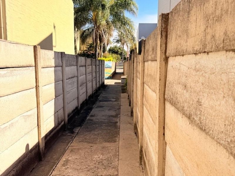 A narrow exterior walkway between two concrete boundary walls leading towards the rear of the property.