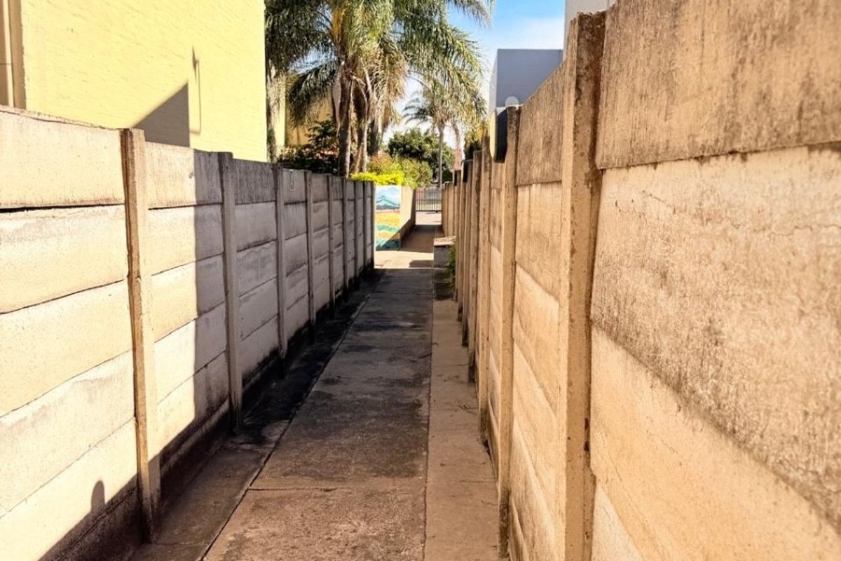 A narrow exterior walkway between two concrete boundary walls leading towards the rear of the property.