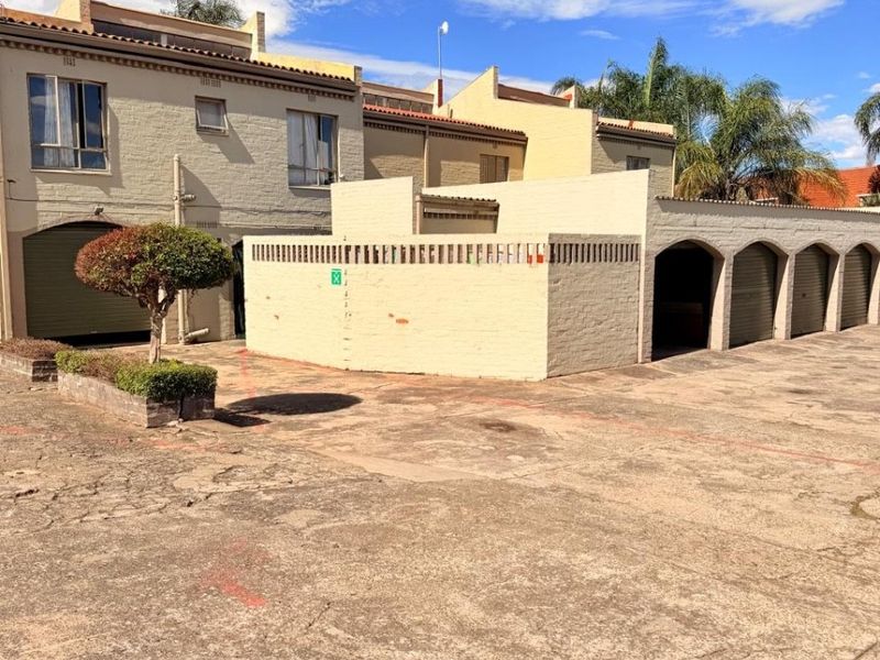 Exterior view of the apartment complex featuring a paved driveway, multiple garage units, and a low-walled courtyard area.
